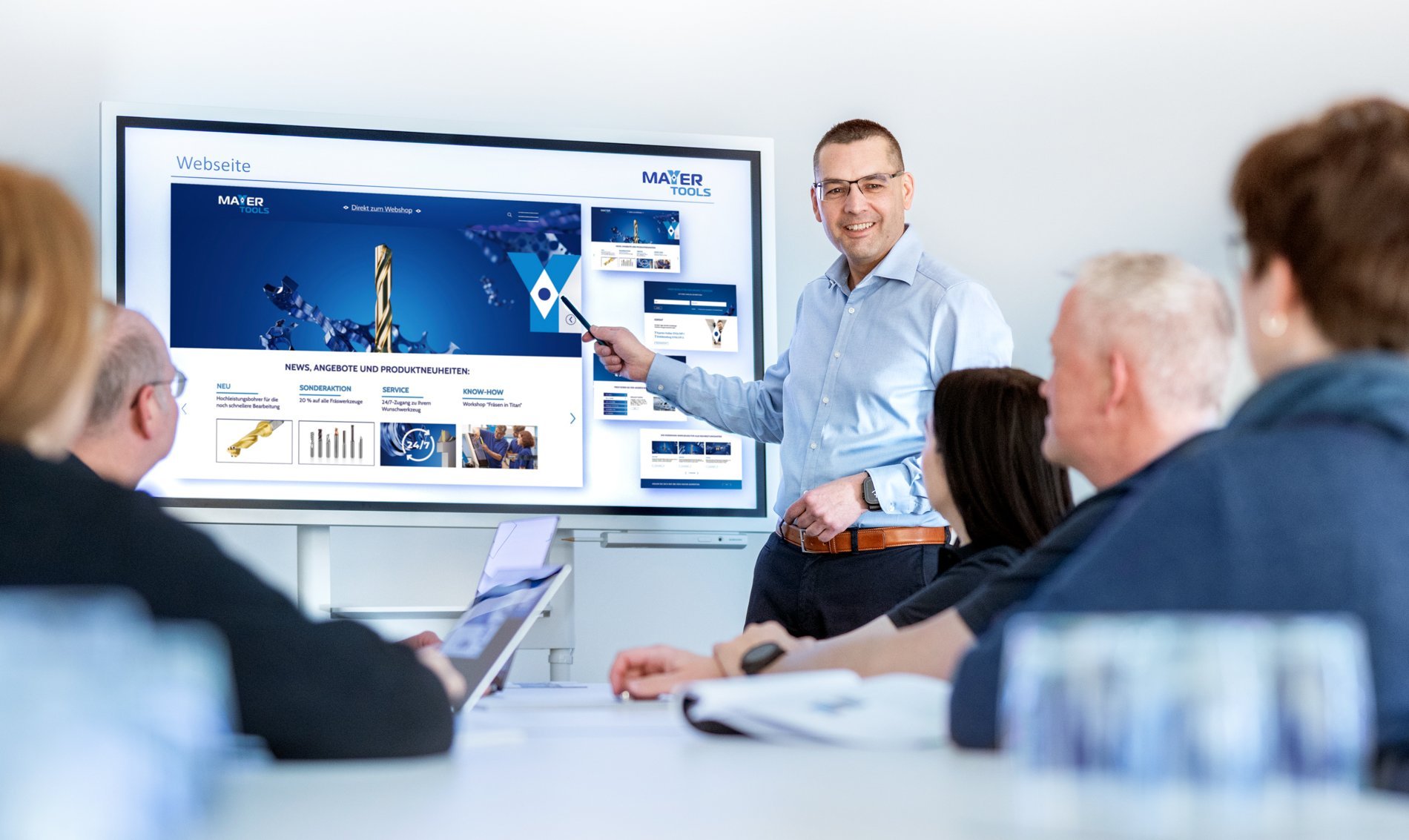 Besprechungsszene im Konferenzraum: Roland Mayer stellt seinem Team die neue Website vor