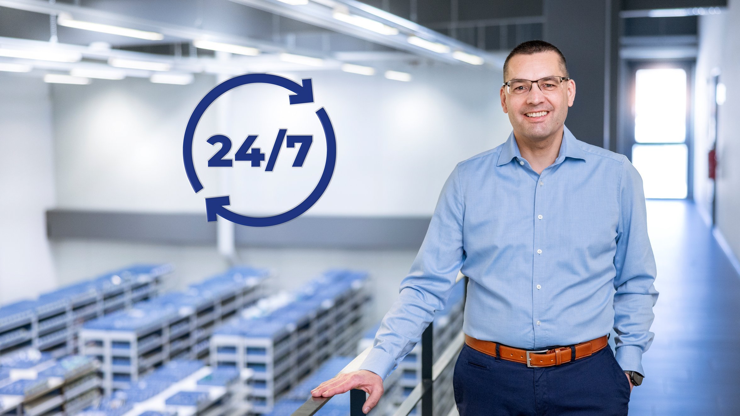 Roland Mayer steht auf dem Gang über dem Werkzeuglager. Unten sind viele Regale mit Werkzeugbehältern zu sehen. Daneben der Hinweis 24/7