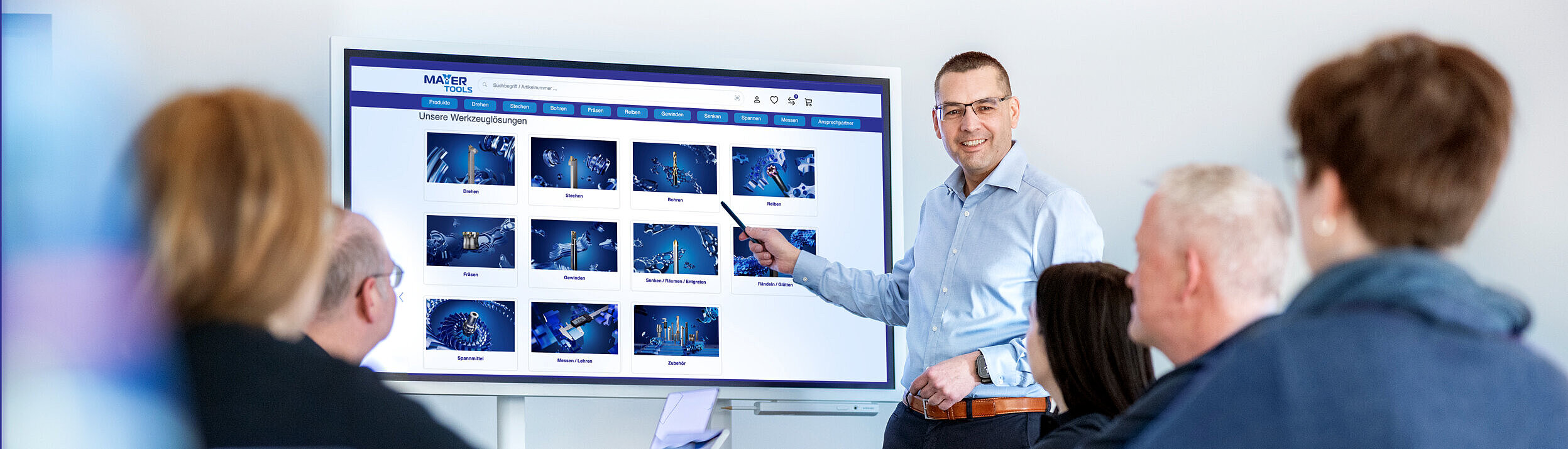 Roland Mayer erklärt einer Gruppe von Personen den eShop an einem großen Monitor.