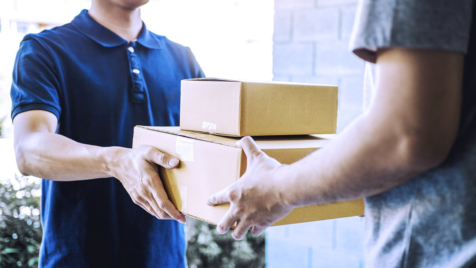 Ein Mann übergibt zwei aufeinander gestapelte Pakete an einen anderen Mann.