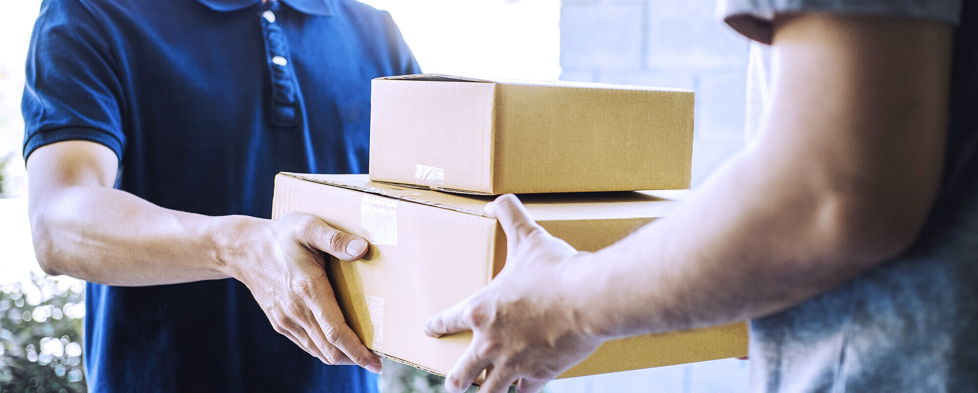 Ein Mann übergibt zwei aufeinander gestapelte Pakete an einen anderen Mann.