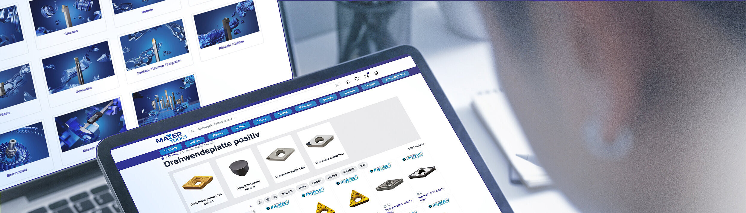 Ein Mann betrachtet einen Werkzeugübersicht im Mayer-eShop auf dem Tablet. Im Hintergrund ist ein Desktop-Monitor mit der Startseite des eShops zu sehen.